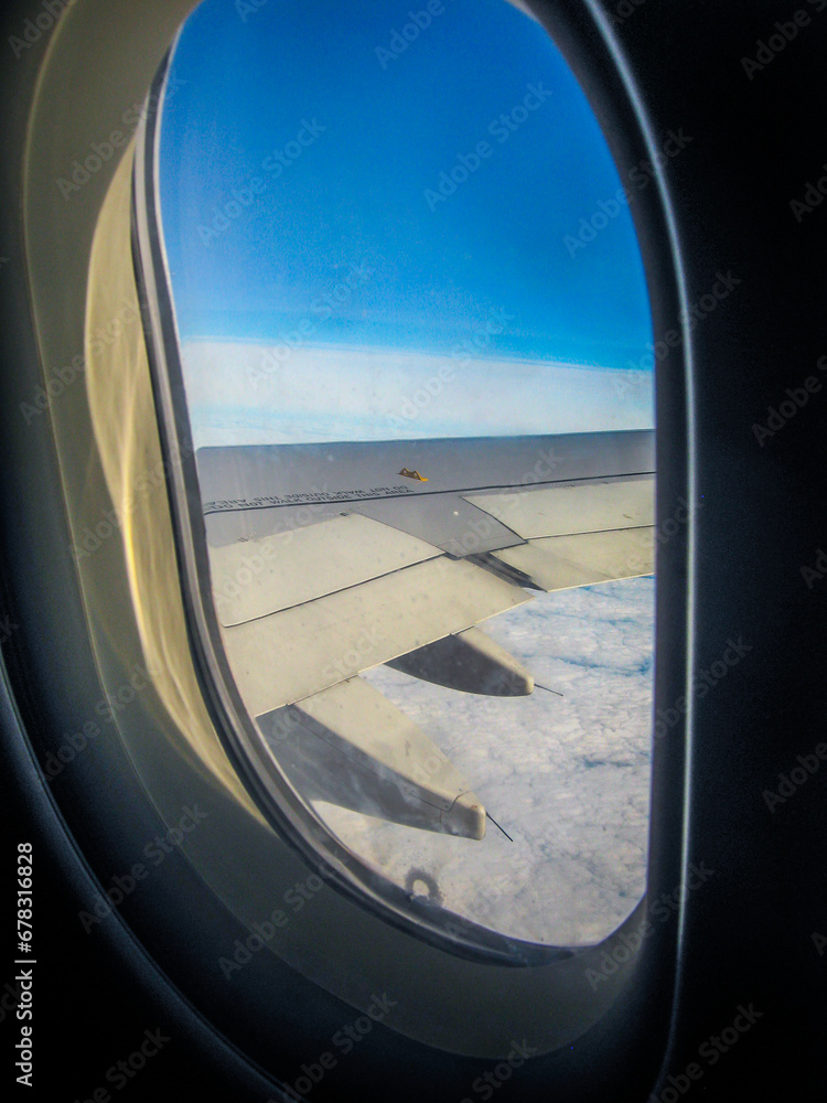 Gray airplane wing in the sky from an oval porthole Gray airplane wing in the sky from an oval porthole