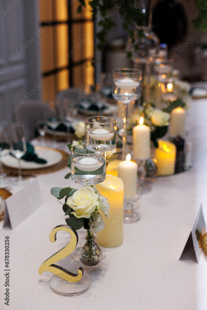 Wedding decorations. Served wedding table with decorative fresh white flowers, candles. Celebration details. Flower composition roses, plates, candles in candlesticks and green napkins
