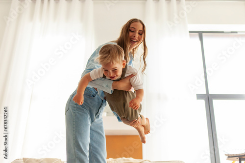 young mother dances with her little son at home and holds hands, woman plays with her child in the room