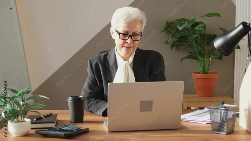 Confident stylish european middle aged senior woman using laptop at workplace. Stylish older mature 60s gray haired lady businesswoman sitting at office table. Boss leader teacher professional worker Confident stylish european middle aged senior woman using laptop at workplace. Stylish older mature 60s gray haired lady businesswoman sitting at office table. Boss leader teacher professional worker