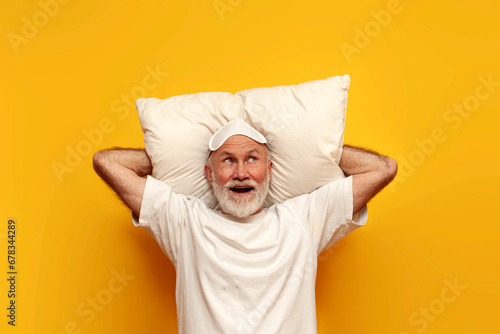 old bald grandfather in pajamas and sleep mask lies on pillow and imagines on yellow isolated background photo