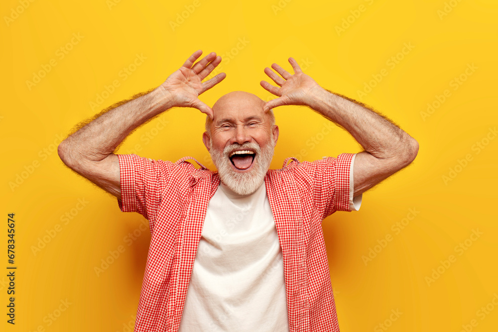joyful old grandfather in summer shirt fooling around and making faces on yellow isolated background - obrazy, fototapety, plakaty 