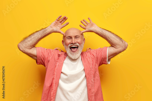 joyful old grandfather in summer shirt fooling around and making faces on yellow isolated background photo