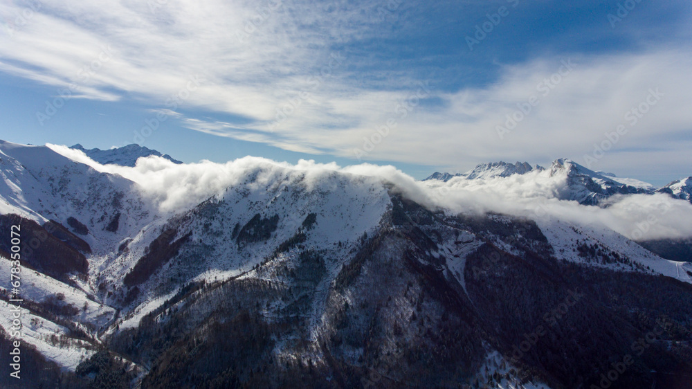 Obraz premium Clouds falling over a snowy mountain aerial sunny day