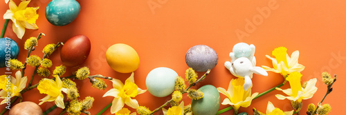 Photography Top view of natural dyes dyed Easter eggs on orange background, yellow daffodils