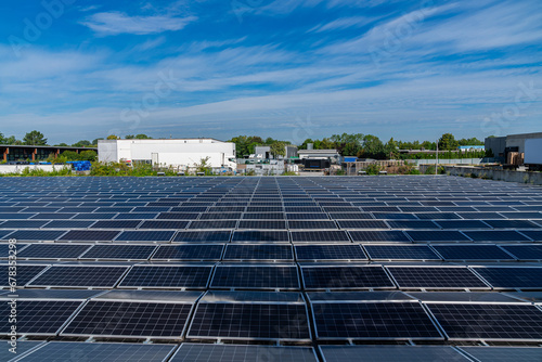 View of multiple solar panels in an industrial area. Blue sky with light clouds.