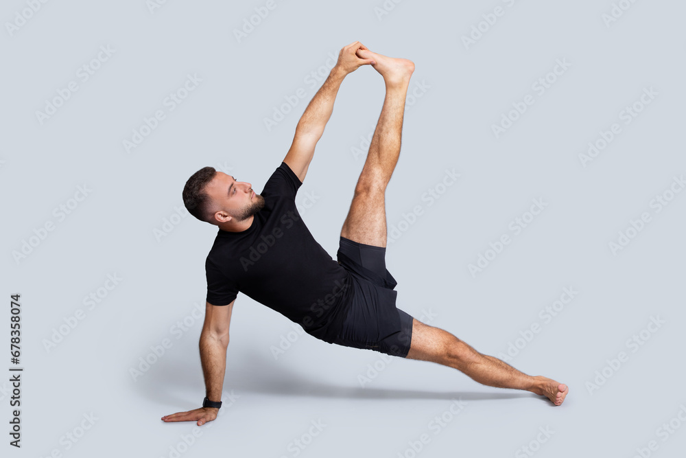 Obraz premium Serious millennial caucasian man in sportswear practice yoga, stretching leg