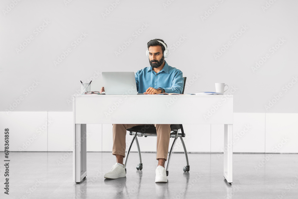 Focused indian man with headphones at laptop Focused indian man with headphones at laptop