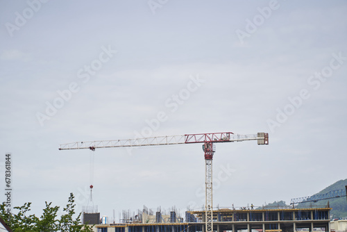 Tall tower cranes on a building under construction against the sky and white clouds. Construction concept. High quality photo