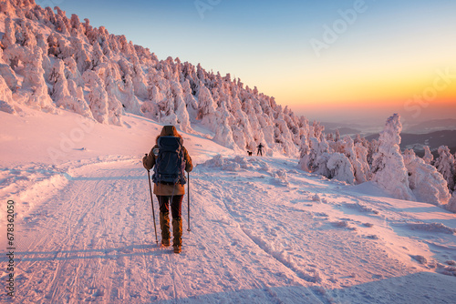 Hiking in snow at winter mountain during sunset. Woman with backpack and nordic walking poles trekking in cold weather. Sports and outdoors seasonal activity