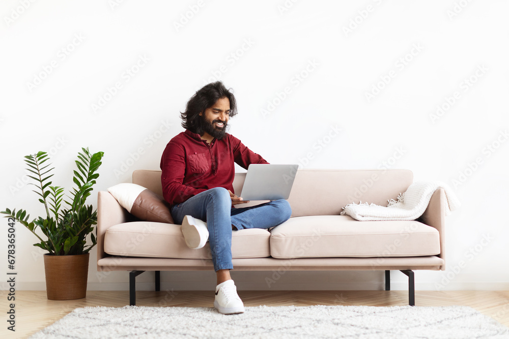 Smiling Indian Man Sitting On The Couch Working On Laptop Smiling Indian Man Sitting On The Couch Working On Laptop