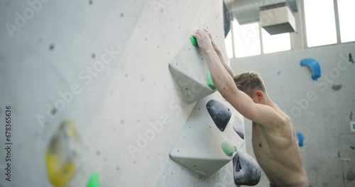 Fit young man using hand and footholds to climb up an artificial wall in a bouldering gym photo