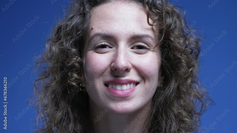 Portrait of a happy young woman smiling at camera on blue backdrop. Female 20s person with curly hair Portrait of a happy young woman smiling at camera on blue backdrop. Female 20s person with curly hair