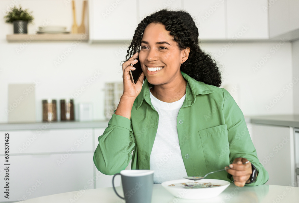 African Lady Communicating On Smartphone While Having Breakfast In Kitchen African Lady Communicating On Smartphone While Having Breakfast In Kitchen