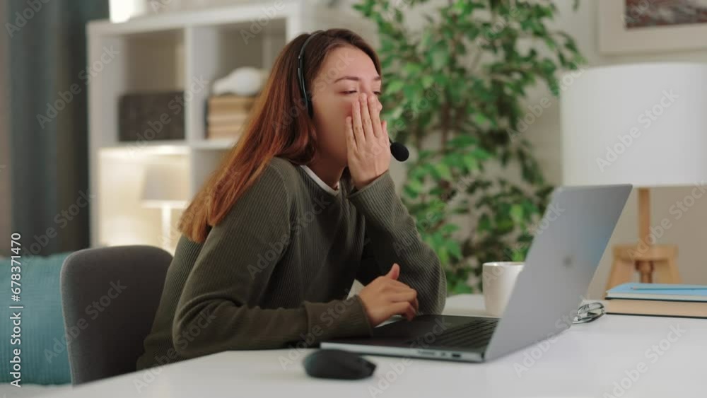 Young tired sleepless female freelancer talking on laptop with headset, giving advice, woman yawning and drinking morning coffee to cheer up Young tired sleepless female freelancer talking on laptop with headset, giving advice, woman yawning and drinking morning coffee to cheer up