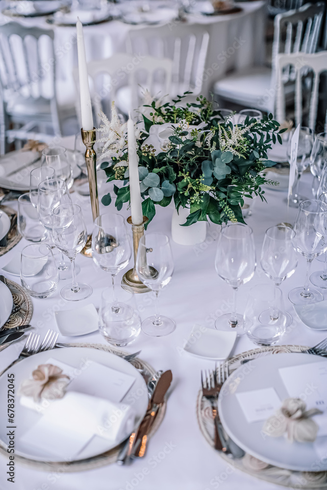 The wedding festive table is decorated with floral arrangements, glasses, plates and cutlery, the table is covered with a beautiful tablecloth