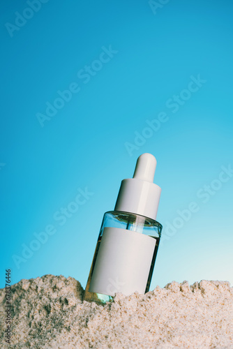 Serum in glass bottle with pipette for the face on blue background and sand texture.copy space. Mock up advertising copy space.