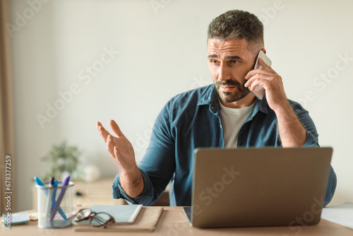 man browses laptop answering unpleasant phone call indoor