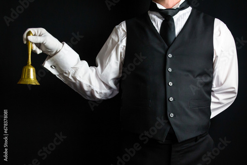 Portrait of Butler or Hotel Concierge Wearing Vest and White Gloves Holding Gold Bell. Concept of Ring for Service.