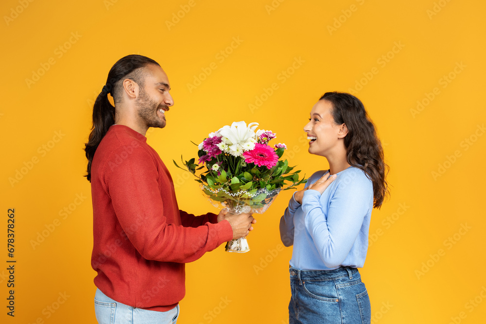 Positive millennial guy gives bouquet of flowers to lady