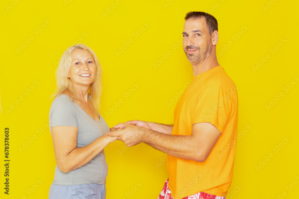 Photo of adorable caucasian couple in their 40s holding arms looking at each other ready to kiss, isolated over yellow background. Photo of adorable caucasian couple in their 40s holding arms looking at each other ready to kiss, isolated over yellow background.