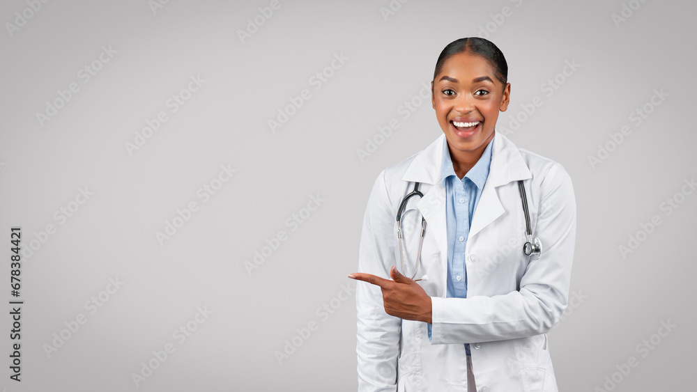 Shocked glad millennial black lady doctor point finger to free space, isolated on gray background Shocked glad millennial black lady doctor point finger to free space, isolated on gray background