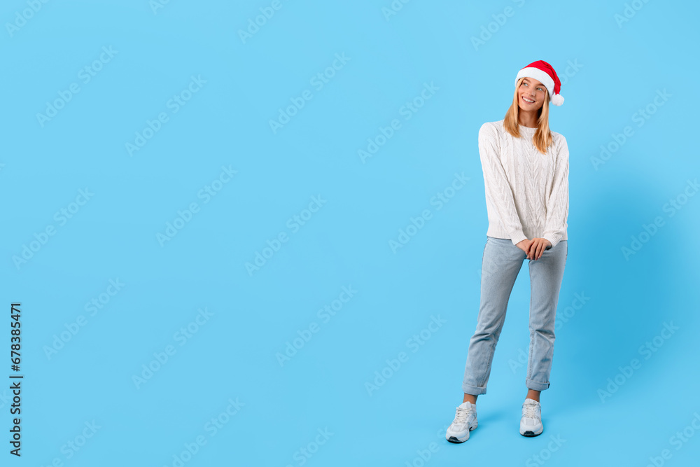 Happy woman in Santa hat posing on blue background, free space
