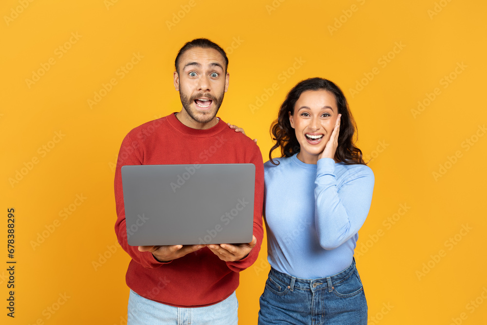 Surprised millennial husband and wife holding laptop Surprised millennial husband and wife holding laptop