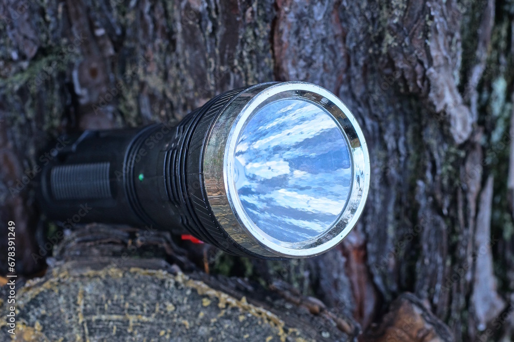 one old black electric flashlight lies on a pine stump on the street in nature one old black electric flashlight lies on a pine stump on the street in nature