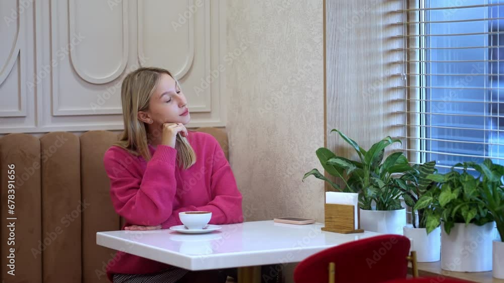 Cute girl with long hair sitting at restaurant table near window and stroking her blonde hair Cute girl with long hair sitting at restaurant table near window and stroking her blonde hair