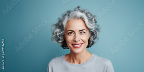 Half-length portrait adult woman, graced with short silvery hair, healthy skin and warmth smile on blue banner background with copy space. Concept skin care, beautiful and glowing aging
