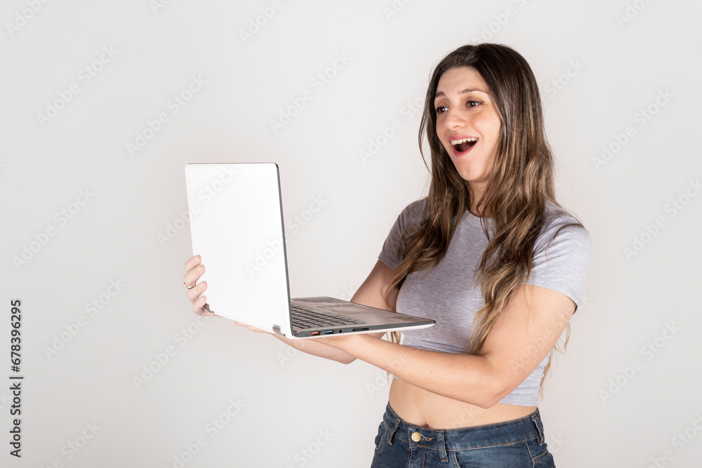 Naklejka premium Studio portrait on white background of blonde woman holding a computer looking at the screen happy and in amazement