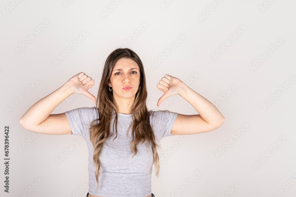 Blonde woman looking at camera with two thumbs down on white studio background. Concept of disapproval Blonde woman looking at camera with two thumbs down on white studio background. Concept of disapproval