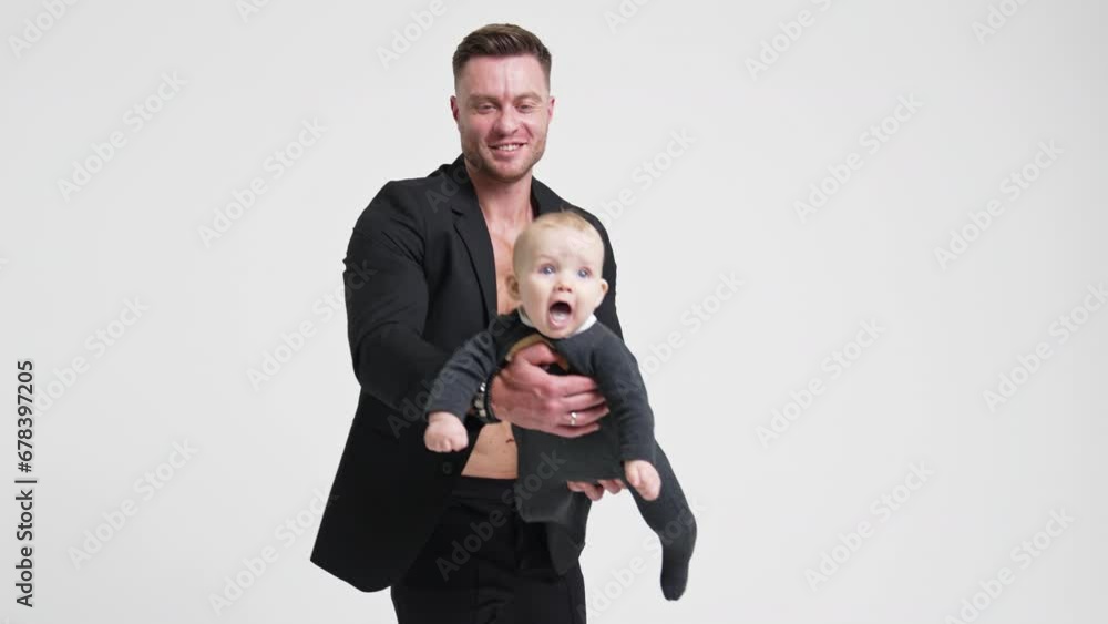 Happy Caucasian dad in black jacket waving his baby boy. Little infant is smiling adorably and father kisses his son. White backdrop. Happy Caucasian dad in black jacket waving his baby boy. Little infant is smiling adorably and father kisses his son. White backdrop.