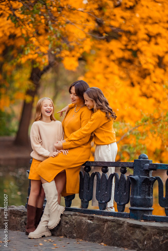 Happy family with teenagers on a walk in the park. a young mother and her twin daughters in knitted autumn clothes are having fun and hugging