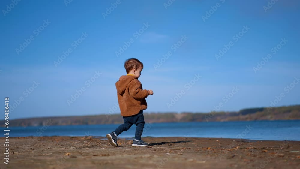 Lovely toddler boy walking to the river. Cute little kid throws the stone into water and walks away. Lovely toddler boy walking to the river. Cute little kid throws the stone into water and walks away.