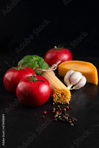 On a dark background, ingredients for cooking spaghetti with tomato sauce and parmesan.