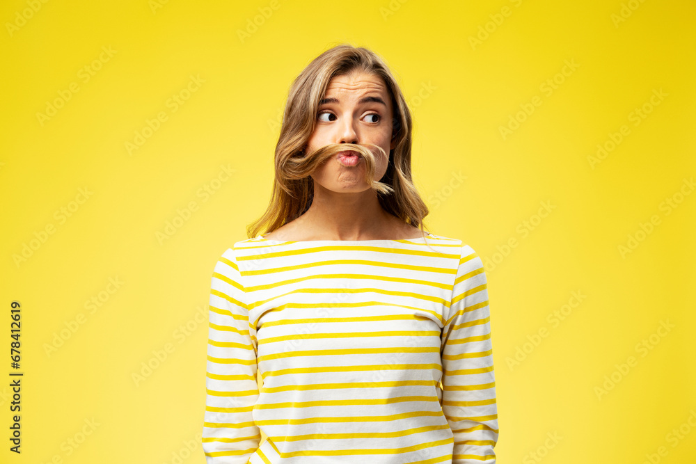 Portrait of happy young woman playing with hair, showing grimace looking away isolated on yellow background. Concept of positive lifestyle - obrazy, fototapety, plakaty 
