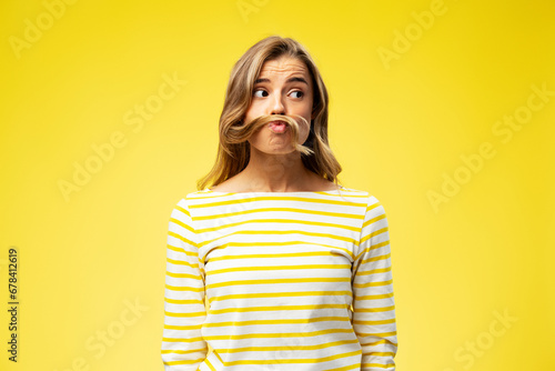 Portrait of happy young woman playing with hair, showing grimace looking away isolated on yellow background. Concept of positive lifestyle photo