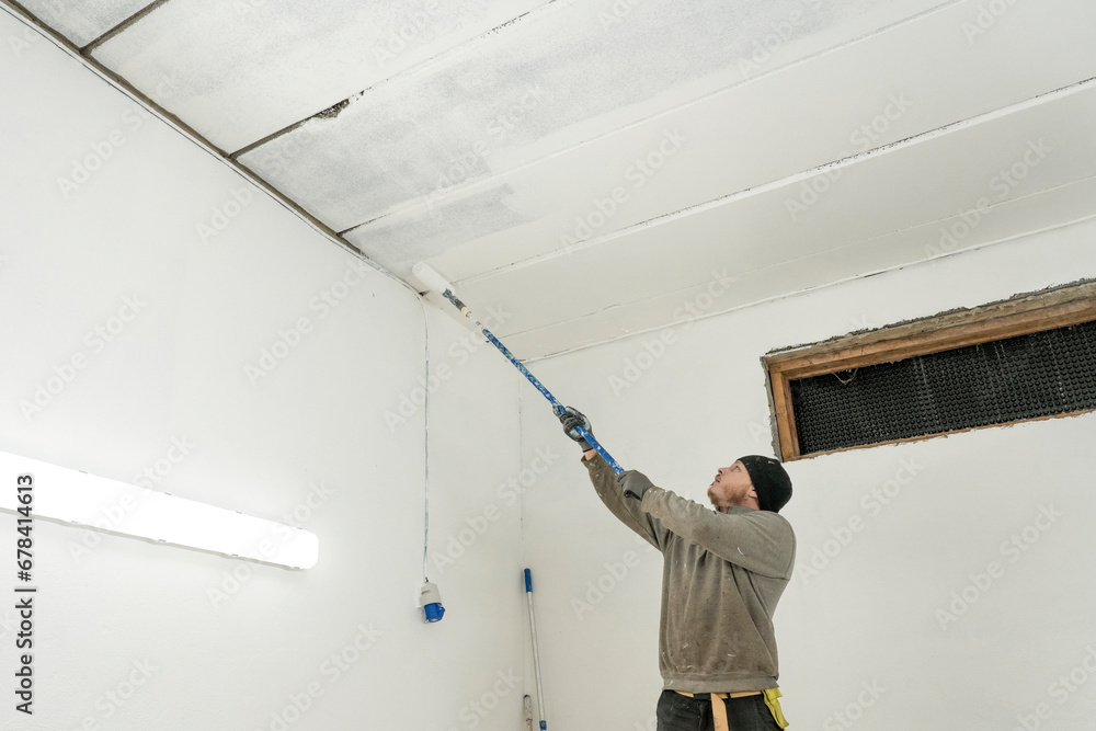 Skilled Worker in Work Attire Paints Interior with Precision Using Roller. Skilled Worker in Work Attire Paints Interior with Precision Using Roller.