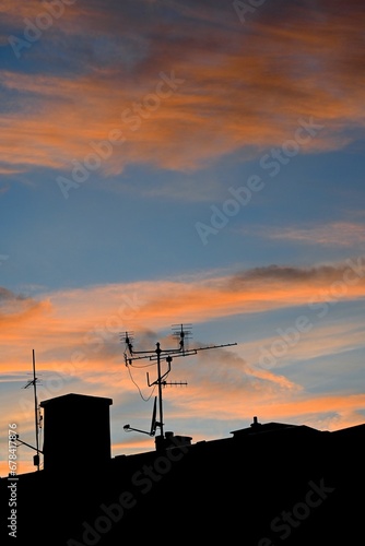 Satellite dish and tv antenna on the roof of a building against a cloudy sky at sunset