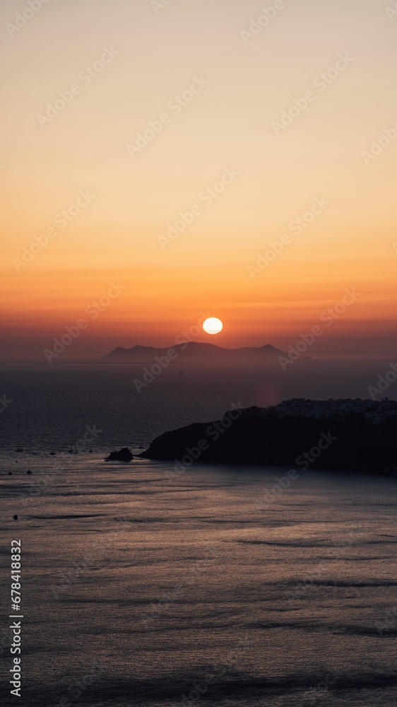 Gorgeous vertical shot of a golden sun over the horizon in Santorini, Greece at sunset