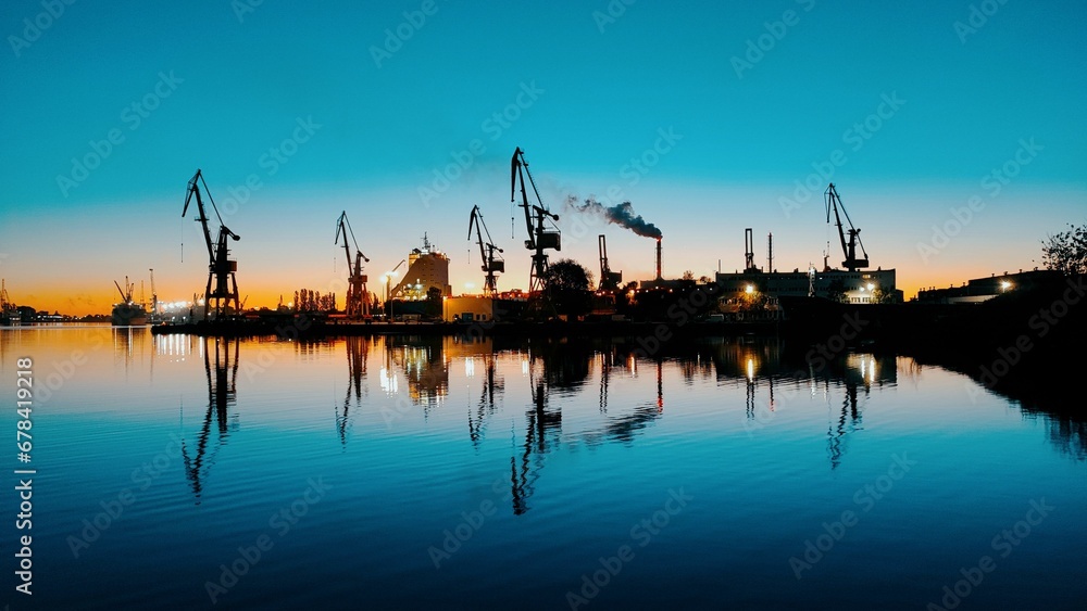 View of cranes at a harbour with vivid blue sky reflected in the water