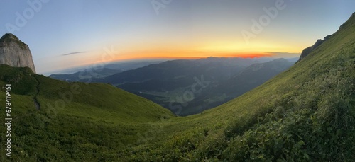 Panoramic view of a sunrise over mountains covered with green grass