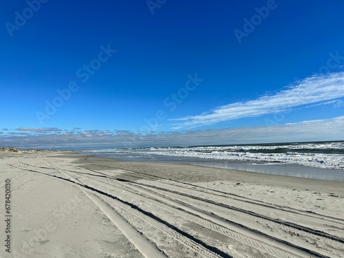 Beach of a wavy sea with wheel prints on the wet sand