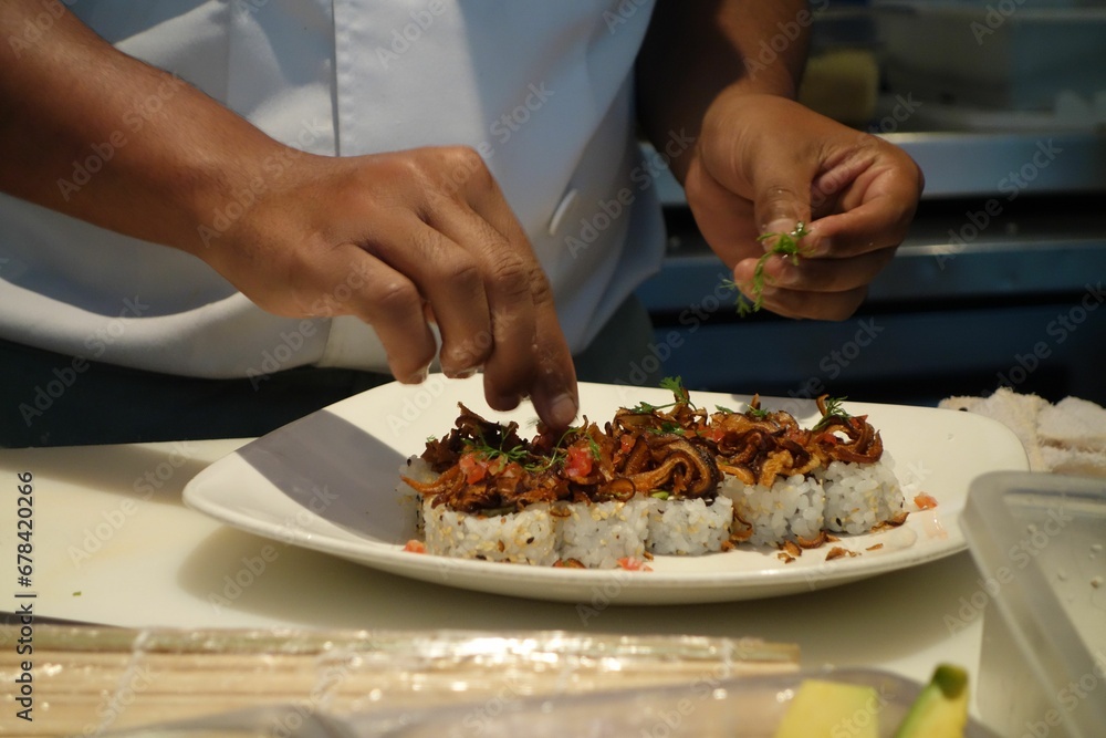 Cook adding some green to the sushi on a round plate