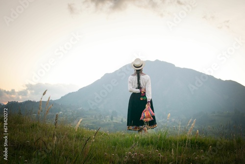Back shot of Saraguro native girl walking wearing traditional regalia looking at a big mountain photo