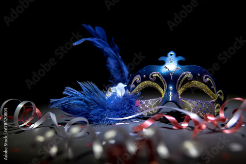 Festive blue and gold venetian carnival mask with streamers and confetti on a black background