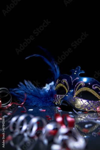 Vertical shoot of a festive blue and gold venetian carnival mask with streamers and confetti on a black background and reflect