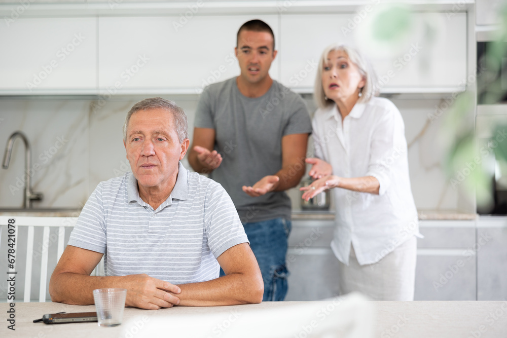 Obraz premium Elderly woman and adult man during family quarrel with elderly man in kitchen